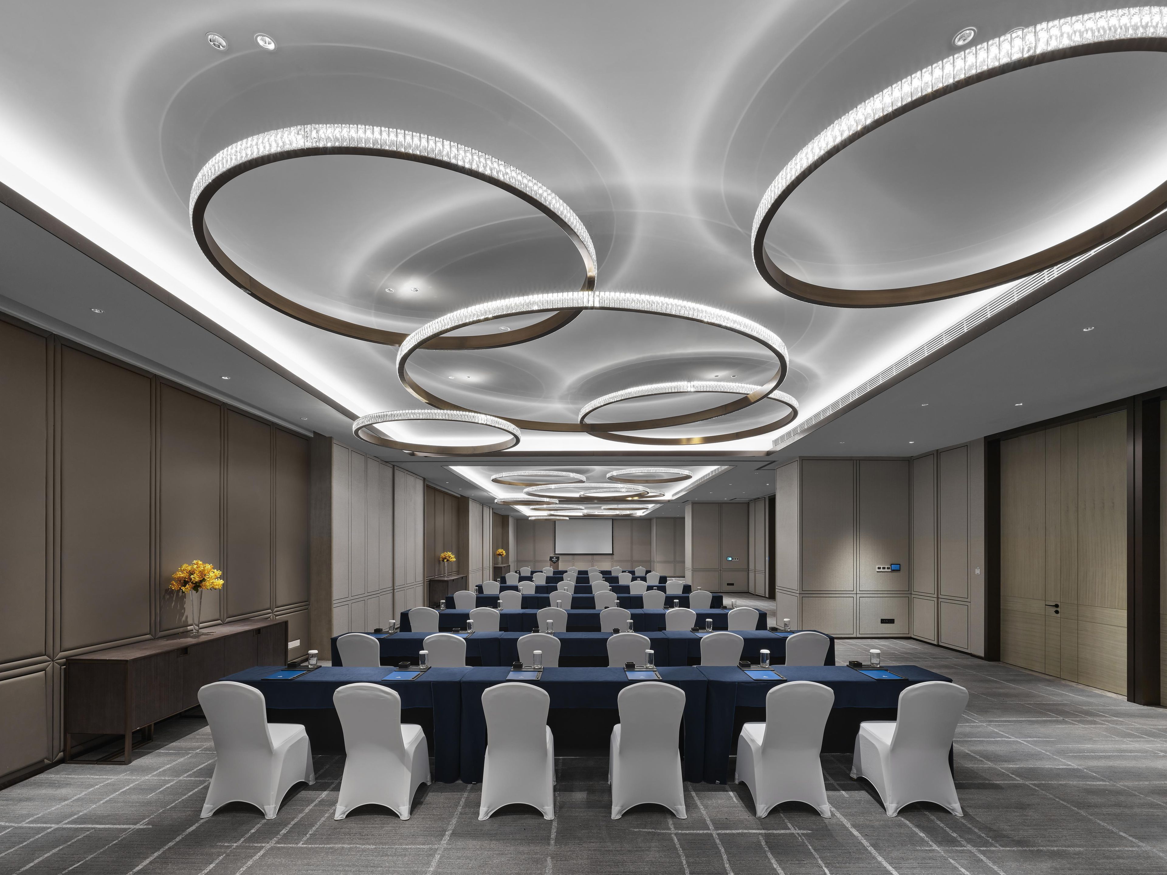 A conference room with a long table, white chairs, and a modern ceiling design.