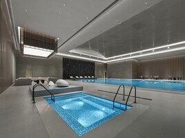 Piscina interior moderna com formato retangular, rodeada por espreguiçadeiras e um espaço de estar com bar junto à piscina.