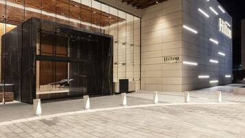 A modern hotel entrance with a glass facade, a prominent 'Hilton' sign, and a clean, tiled pavement.