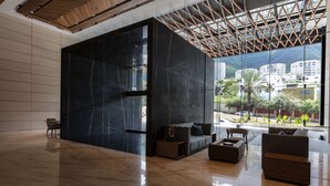 A spacious lobby with a black marble wall, a wooden ceiling, and a view of buildings and greenery outside.