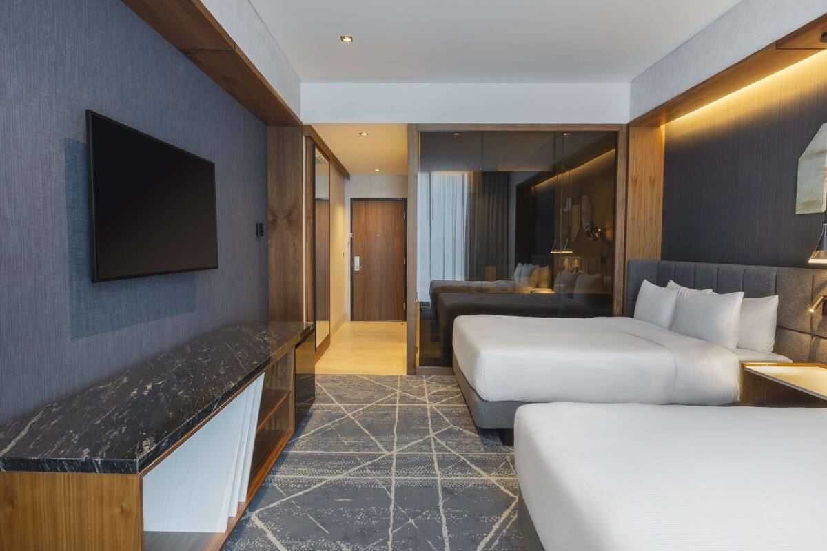 A modern hotel room with a flat-screen TV, two beds, a desk, and a walk-in closet.