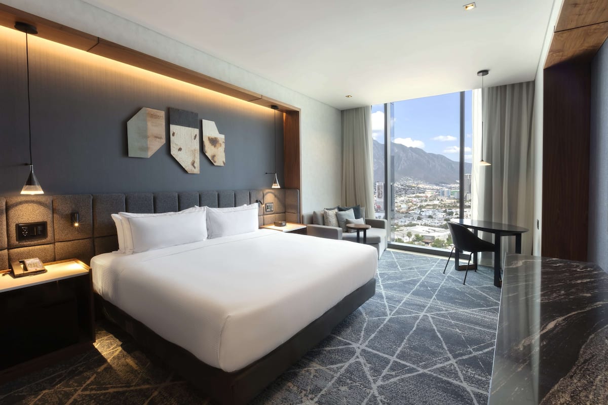 A modern hotel room with a large bed, a desk, and a view of a cityscape.