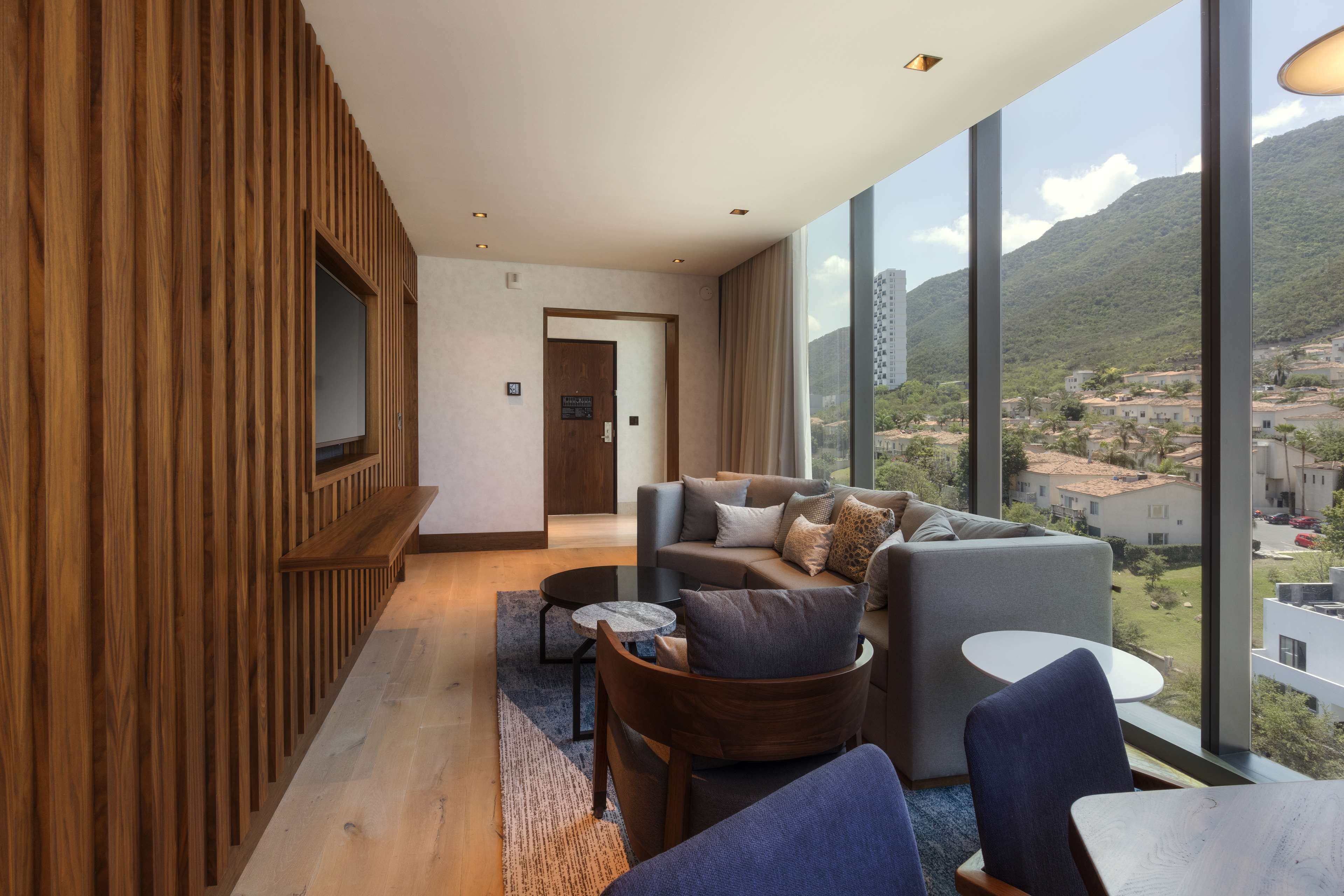 A modern living room with a sofa, chairs, and a view of a mountainous landscape through large windows.
