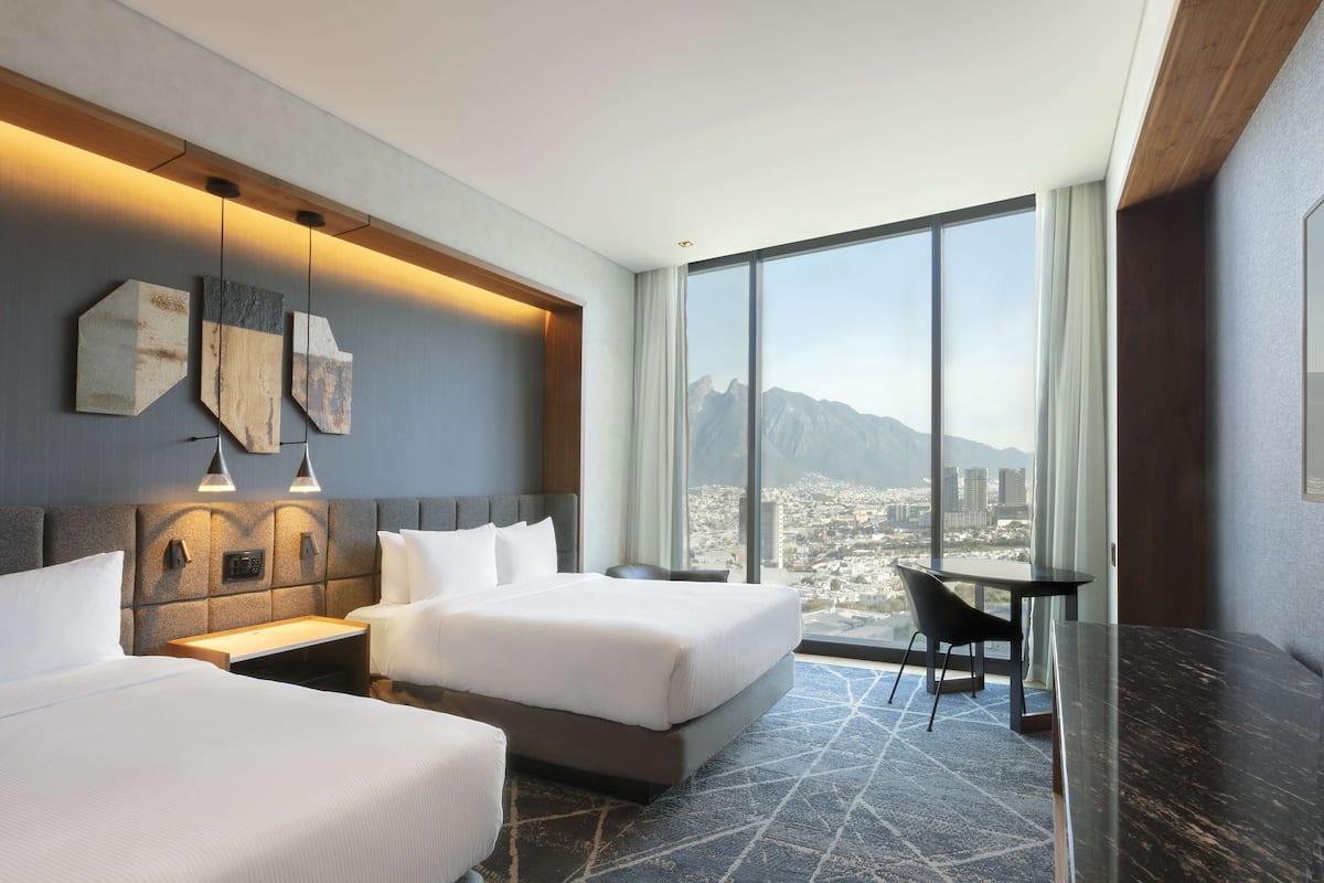 A hotel room with a large window, a bed, a desk, and a chair.