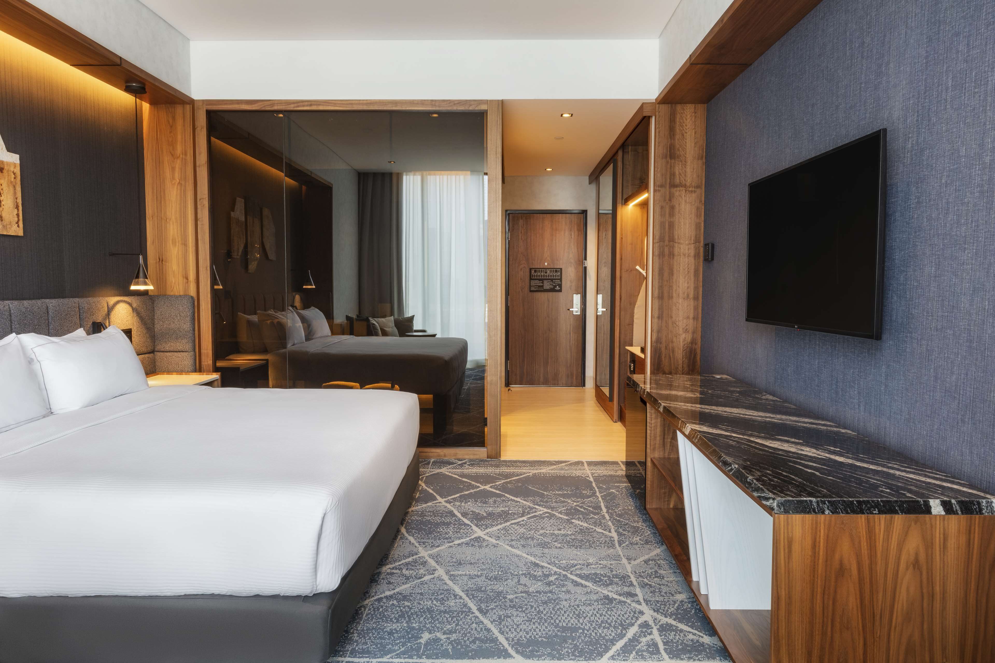 A modern hotel room with a large bed, a desk, a TV, and a walk-in closet.