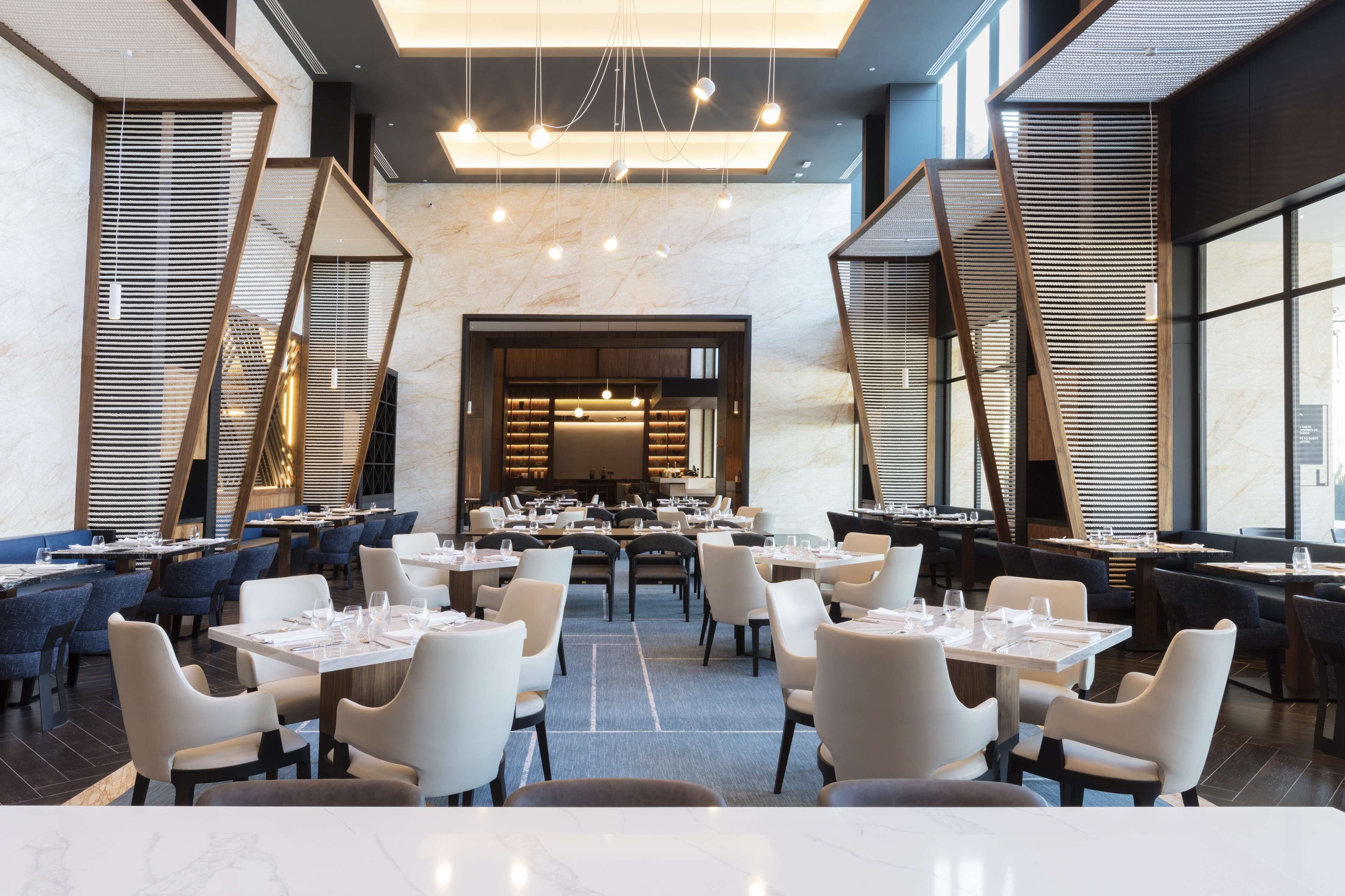 A spacious restaurant with multiple dining tables and chairs, a marble floor, and a modern interior design.