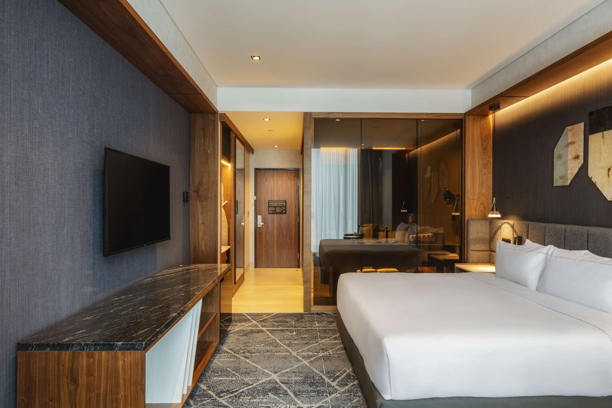 A modern hotel room with a large bed, a flat-screen TV, a desk, and a seating area.