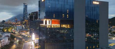 A modern hotel with a glass facade, a prominent Hilton sign, and a view of the surrounding cityscape.