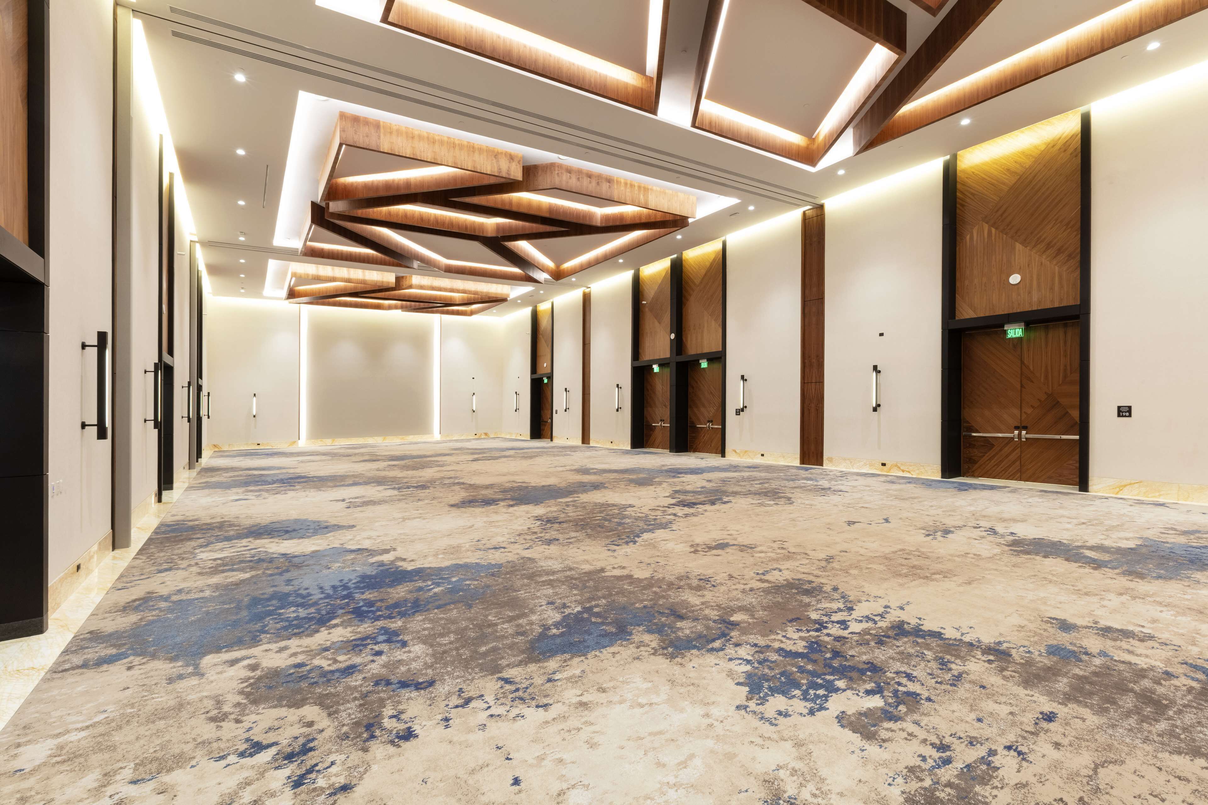 A spacious, modern hotel lobby with a large open area, wooden panel ceiling, and multiple doors leading to rooms.