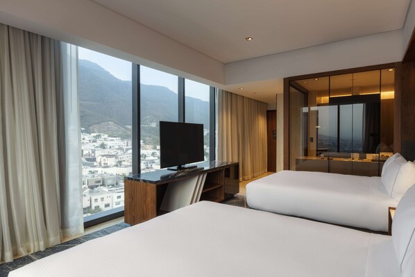 A hotel room with two beds, a TV, and a large window offering a mountain view.