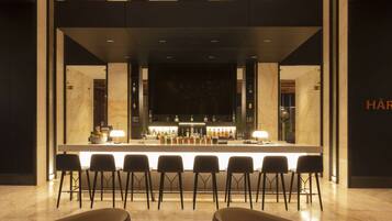 Una zona de bar con encimera de mármol, varias botellas y taburetes.