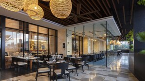 A modern restaurant with a checkered floor, glass partitions, and hanging wicker chandeliers.