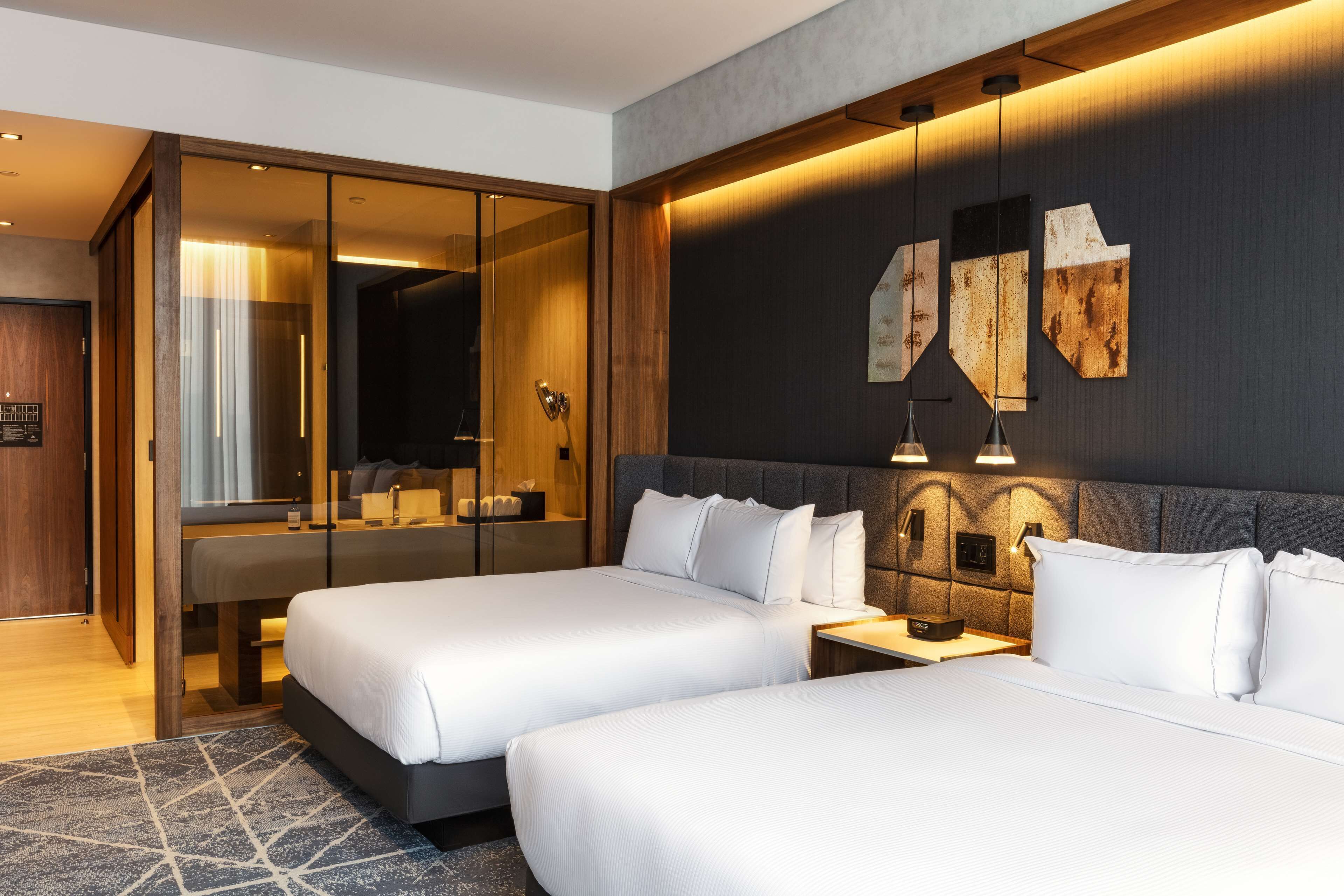 Habitació d'hotel moderna amb dos llits, un mirall gran i una paret decorativa fosca amb obra d'art.