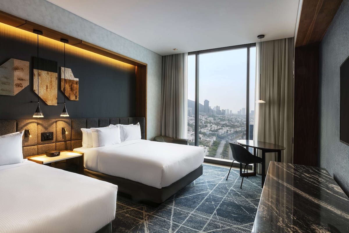 A modern hotel room with a large bed, a desk, and a view of the city.