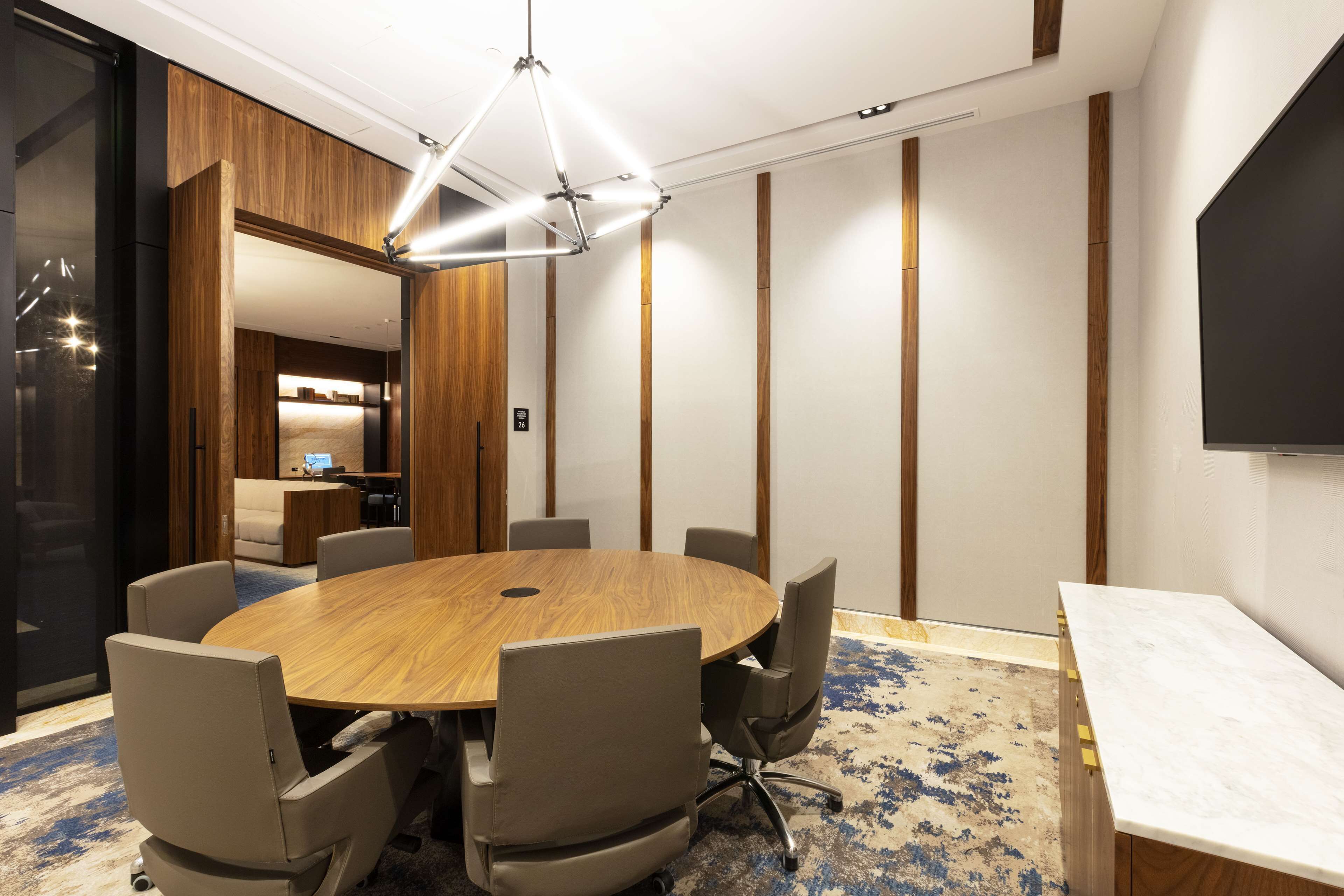 Un salón de conferencias con una mesa redonda de madera, seis sillas, un televisor de pantalla plana grande y una lámpara de araña moderna.