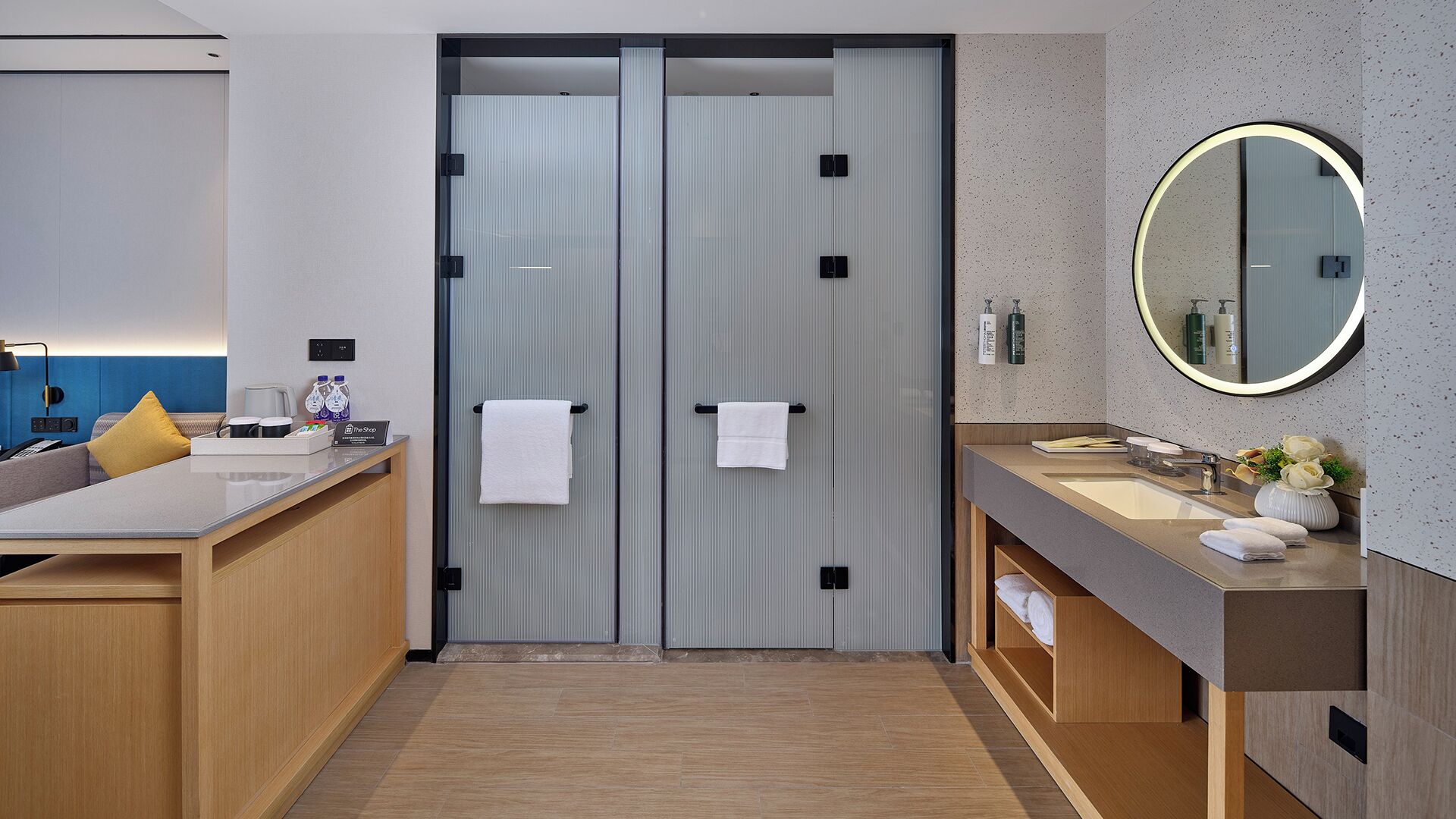 A modern bathroom with a wooden vanity, a round mirror, and a towel rack.