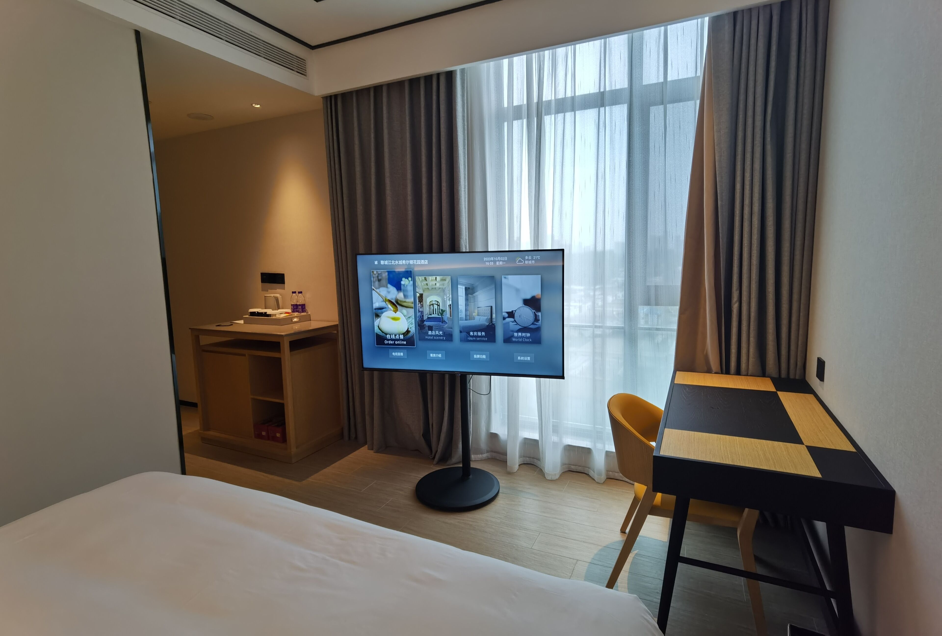 Ein Hotelzimmer mit Bett, Schreibtisch, Fernseher und einem Fenster mit Vorhängen.