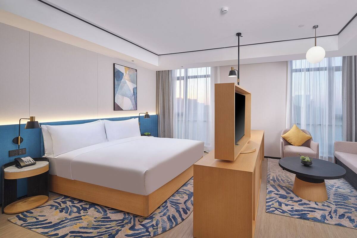 A modern hotel room with a large bed, a sofa, a TV stand, and a coffee table.