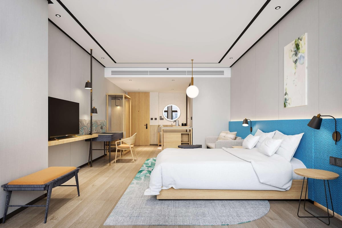A modern hotel room with a bed, desk, chair, and a TV.