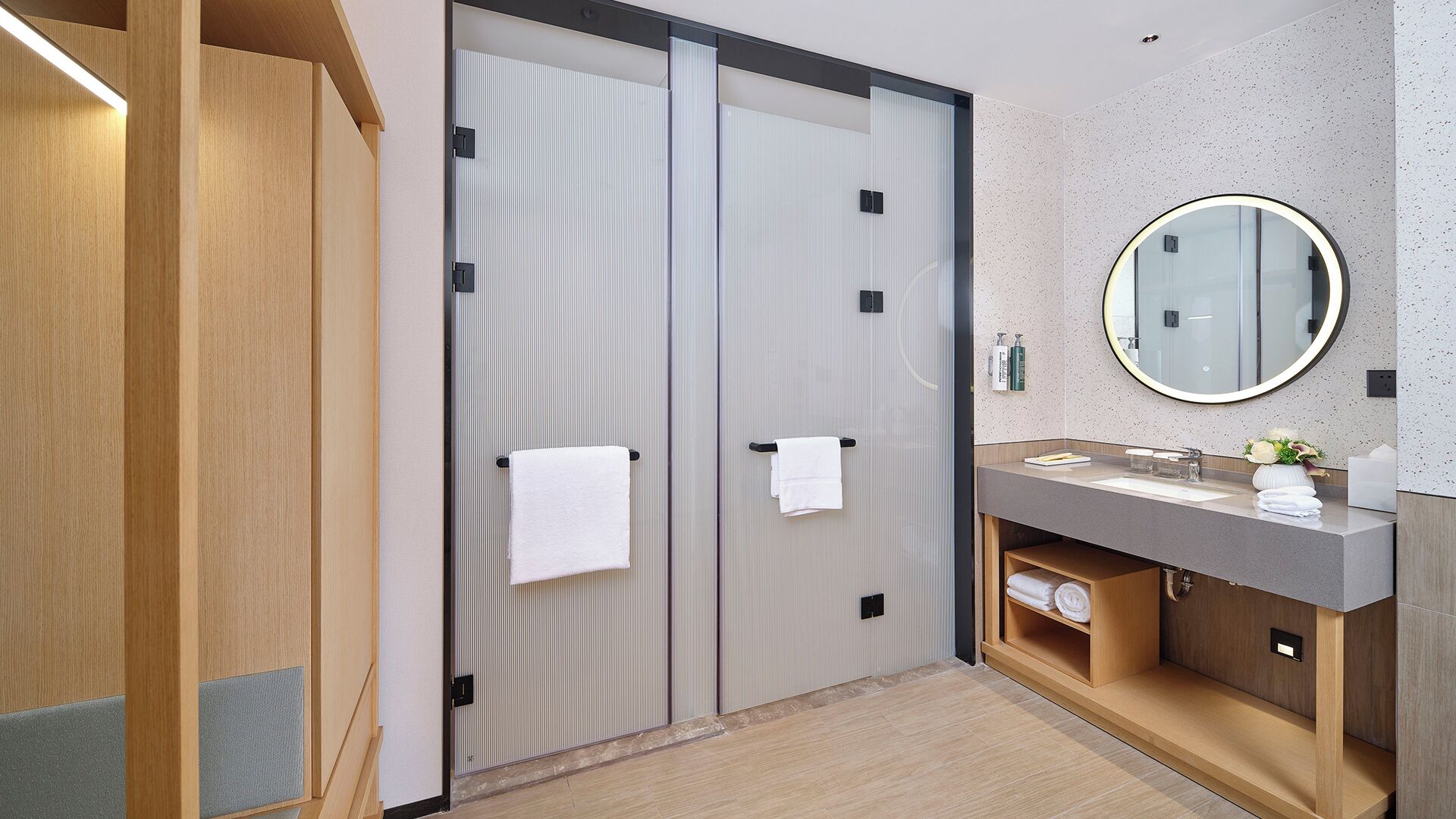 A modern bathroom with a wooden vanity, a round mirror, and two sliding doors.