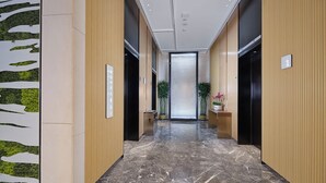 A modern hallway with a marble floor, wooden paneling, and a glass door at the end. - Hilton Garden Inn Liaocheng Jiangbei Shuicheng (Liaocheng)