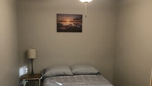 Un dormitorio con cama, mesita de noche, lámpara, ventilador de techo y un cuadro en la pared.