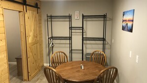 Un comedor con mesa y sillas de madera, una estantería metálica y una puerta de madera.