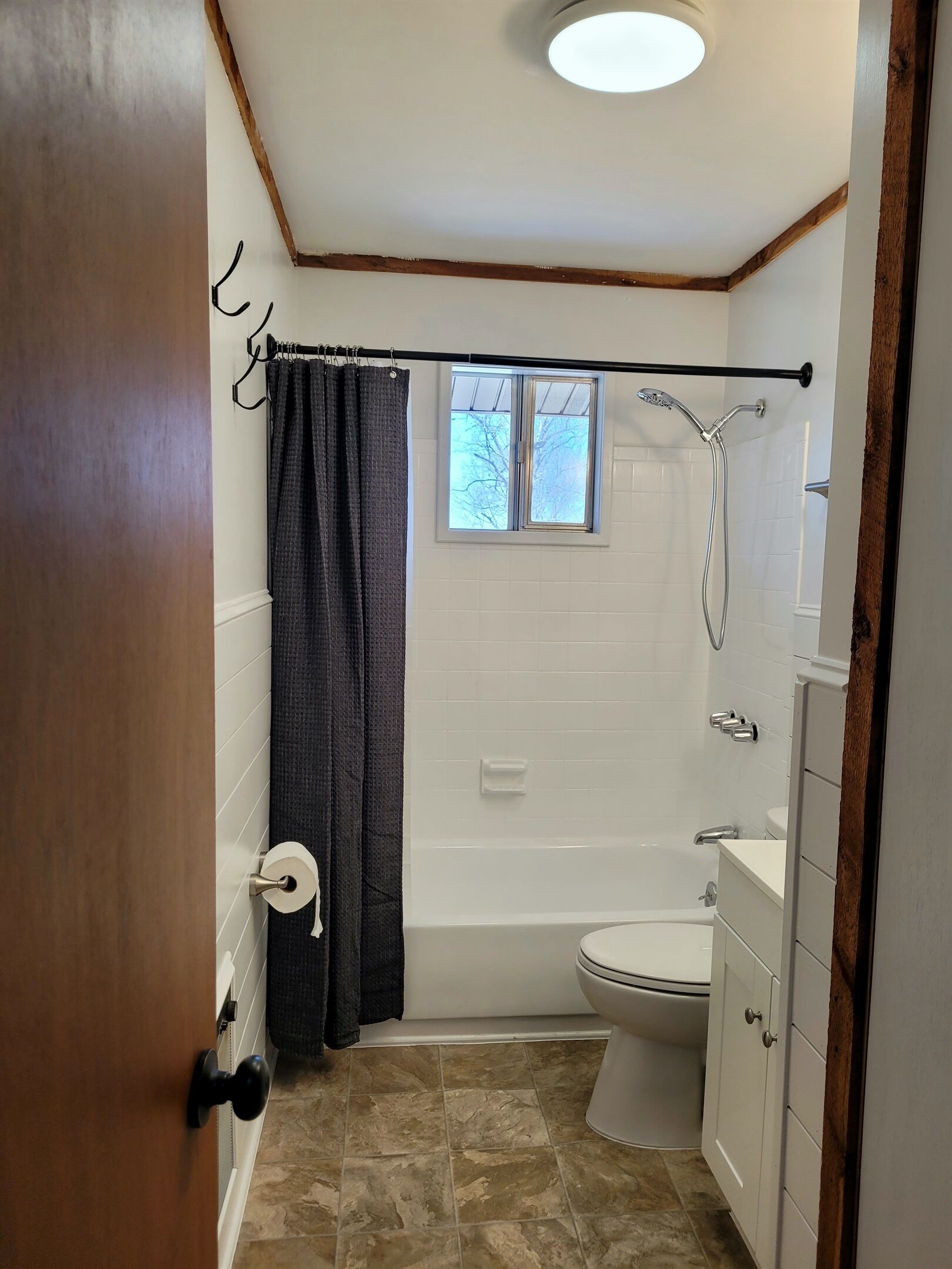 A bathroom with a shower, toilet, and a window.