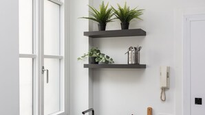 A white door, a window, a wall-mounted phone, and two shelves with plants and kitchen utensils. - Hostmate - Milano - S. Cecilia - Duomo  (Milano)