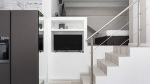 A modern kitchen with a built-in oven, a white wall-mounted TV, and a staircase with a metal railing. - Hostmate - Milano - S. Cecilia - Duomo  (Milano)