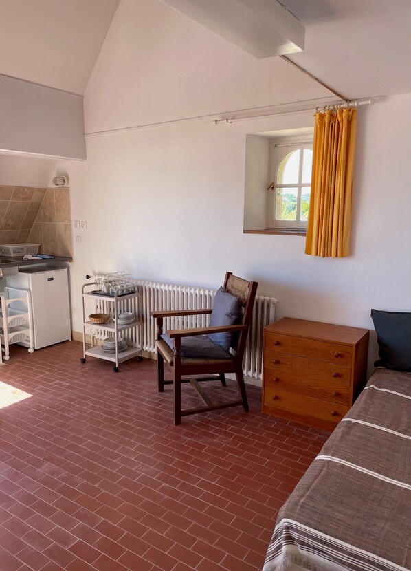 A room with a brick floor, a wooden chair, a wooden dresser, a radiator, and a window with yellow curtains.