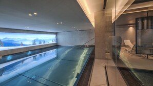 A modern indoor swimming pool with a glass wall and a view of snowy mountains. - Stallion d15 MEGEVE (Megève)
