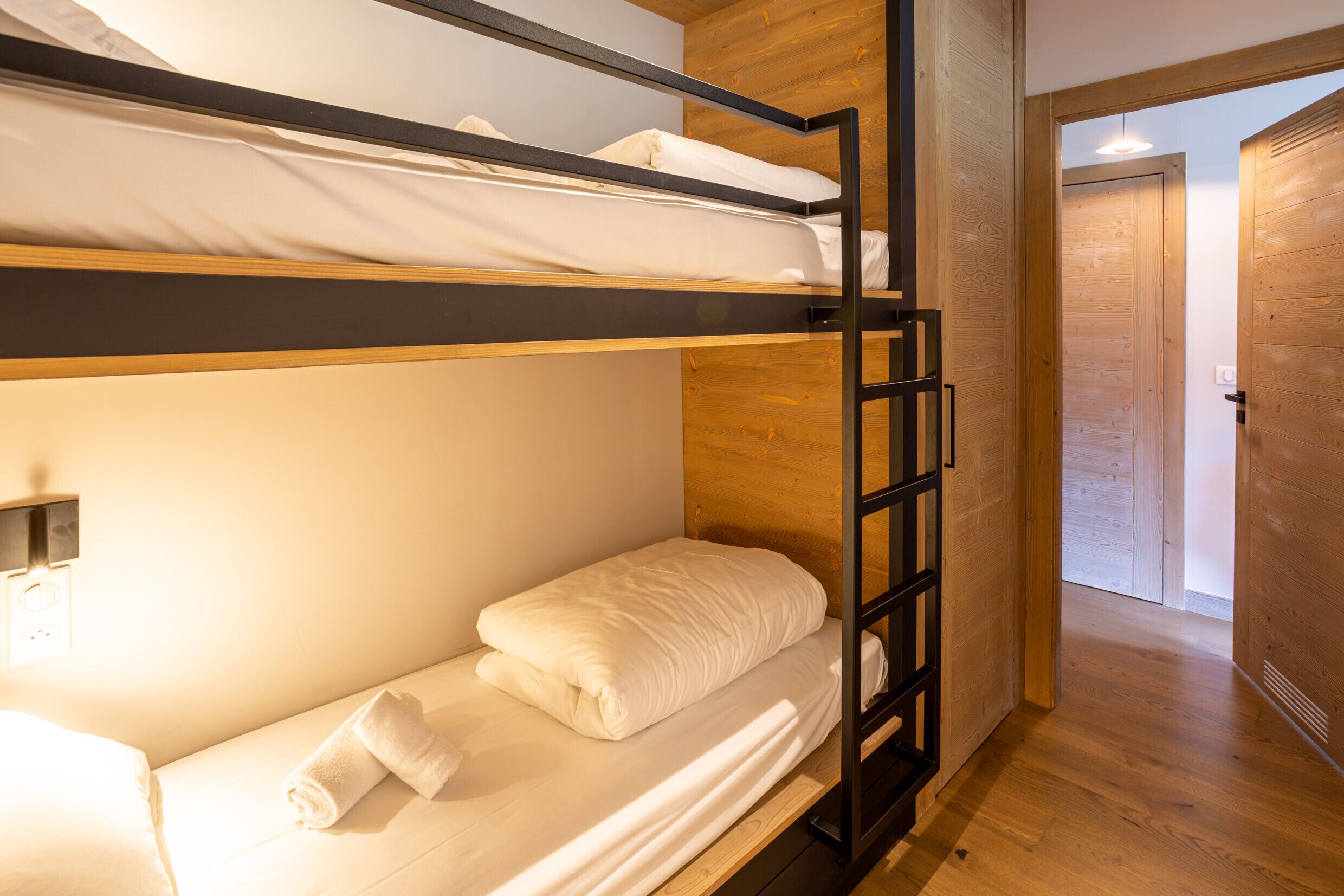 A bunk bed room with a wooden floor and a door in the background.