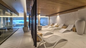 A modern spa area with reclining chairs, wooden stools, and a glass wall offering a view of a snowy landscape. - Stallion d15 MEGEVE (Megève)