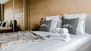 A neatly made bed with a fluffy blanket, grey and white pillows with mountain designs, and a wooden headboard. - Stallion d15 MEGEVE (Megève)