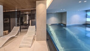 Et moderne poolområde indendørs med to liggestole og en glasafskærmning.