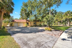 A residential property with a garage, a driveway, and a lawn with palm trees.
