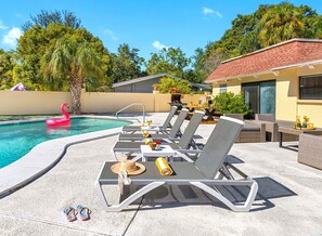 A poolside area with lounge chairs, a flamingo float, and a barbecue grill.