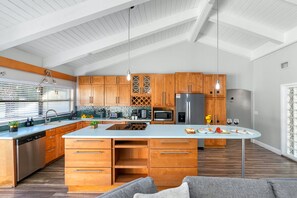 A modern kitchen with wooden cabinets, a large island, stainless steel appliances, and a view of the outdoors.