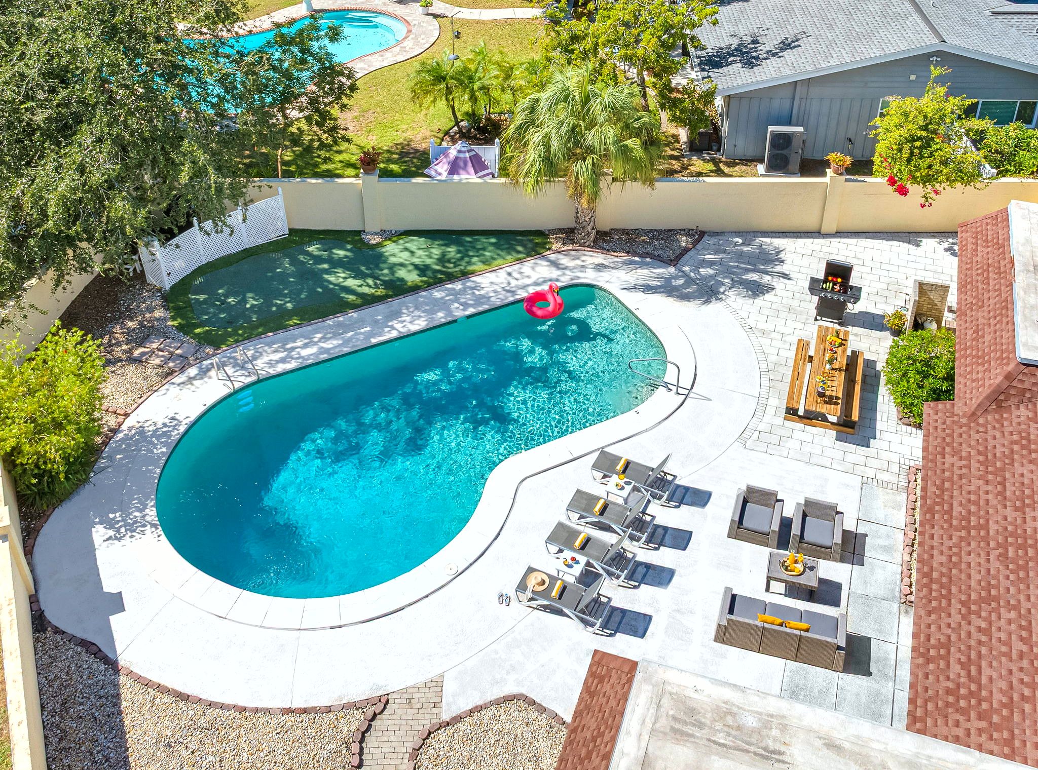 A backyard with a swimming pool, lounge chairs, and a barbecue area.