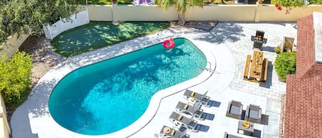 A backyard with a swimming pool, lounge chairs, and a barbecue area.