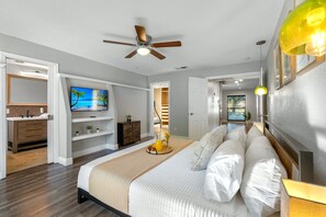 A bedroom with a bed, a ceiling fan, a TV, and a bathroom with a sink and mirror.
