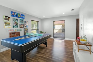 A pool table in a room with wooden flooring, a window with blinds, and various posters on the wall.