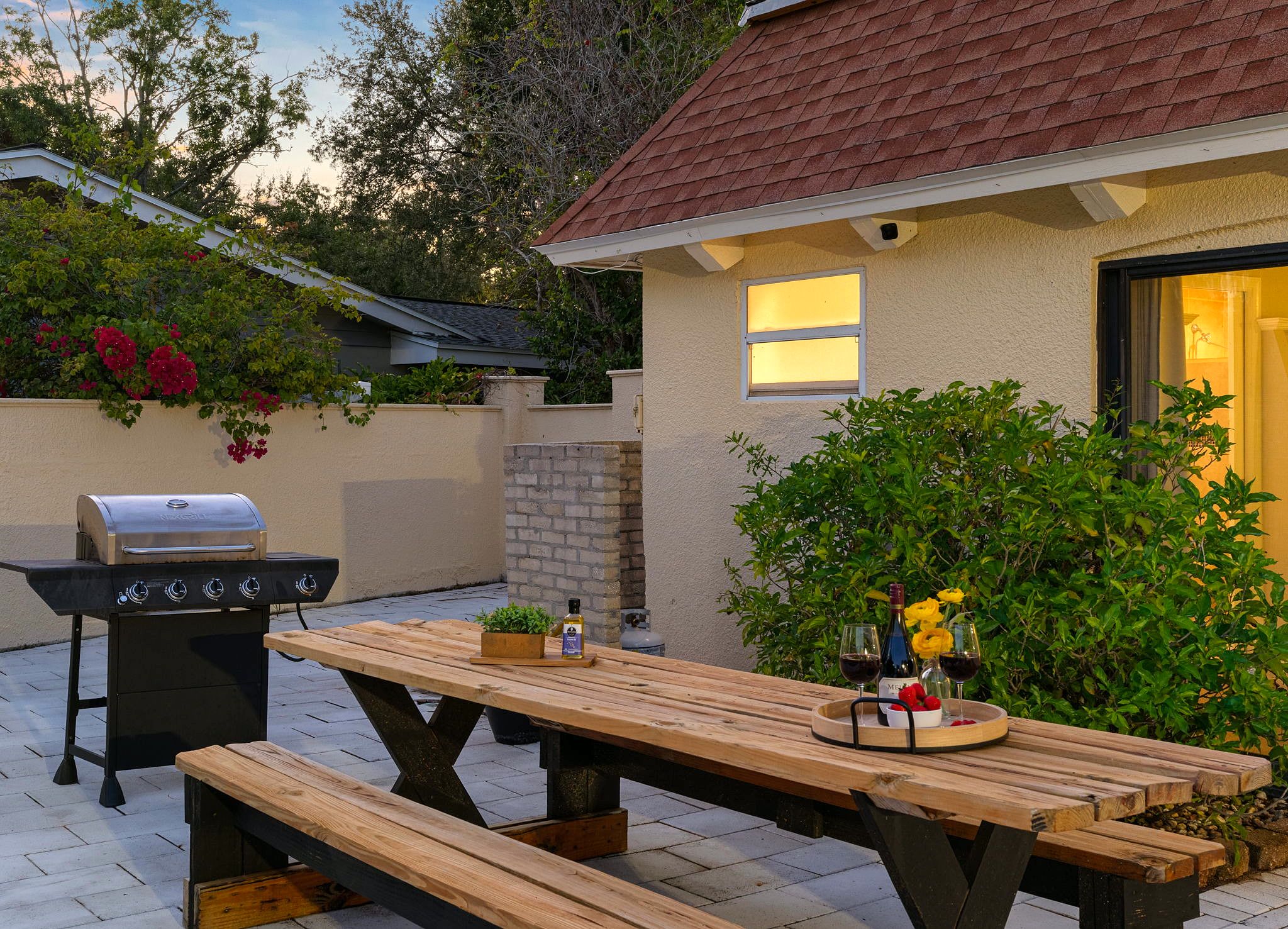 An outdoor patio with a wooden table, a barbecue grill, and a potted plant.