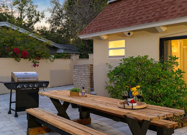Un patio exterior con mesa de madera, una parrilla y una planta en maceta.