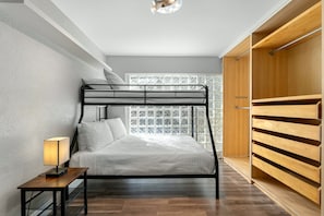 Una cama litera con una mesita de noche y una lámpara, un armario de madera y un ventanal con detalles decorativos.