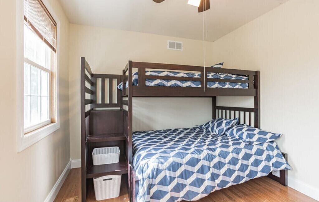 A bunk bed room with a window, wooden ladder, and a ceiling fan.