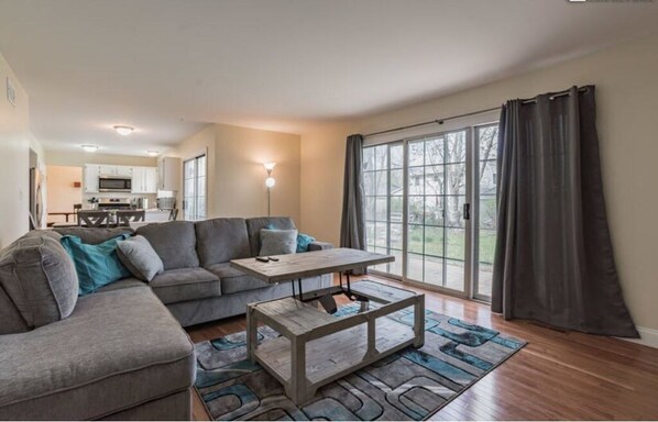 A modern living room with a sectional sofa, a wooden coffee table, and a large sliding glass door leading to a balcony. - Furnished Private home in Aurora sleeps 9 guests (Aurora)