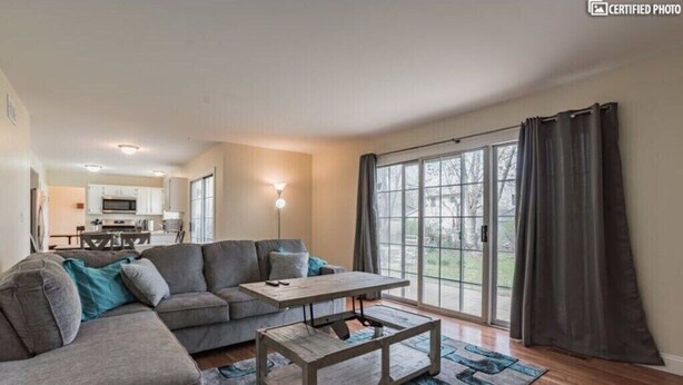 A modern living room with a sectional sofa, a wooden coffee table, and a large sliding glass door leading to a balcony. - Furnished Private home in Aurora sleeps 9 guests (Aurora)