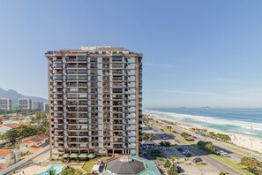 A high-rise hotel with multiple balconies, a swimming pool, and a view of the beach and ocean. - Flat Varandas da Barra- Barra da Tijuca (Rio de Janeiro)